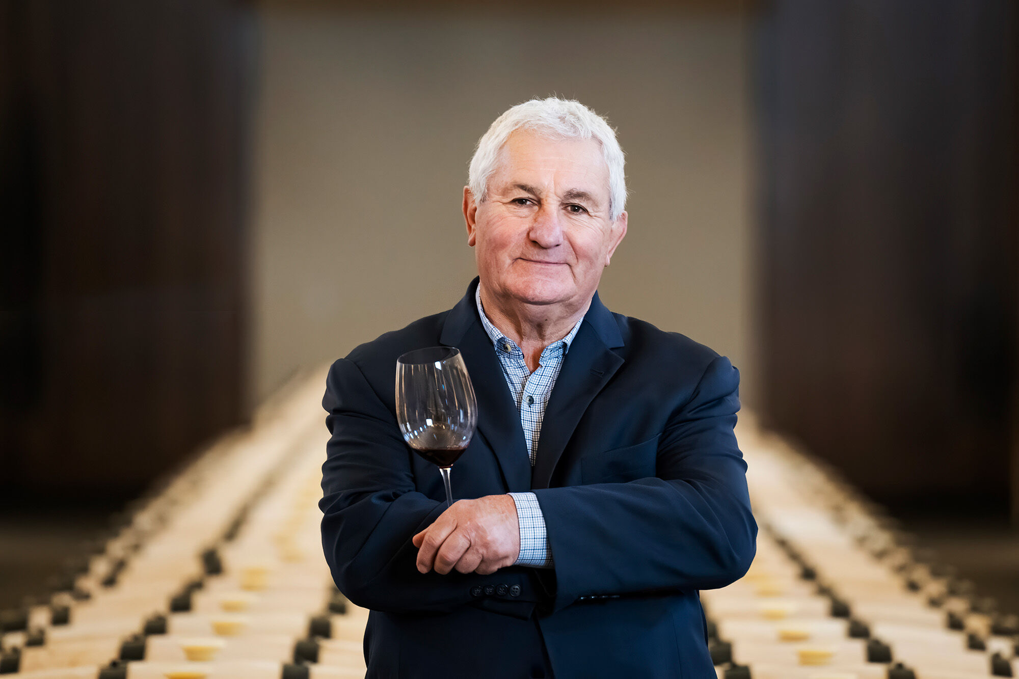 A man in a barrel cellar with a wine glass in hand looking at the camera with a slight smile.