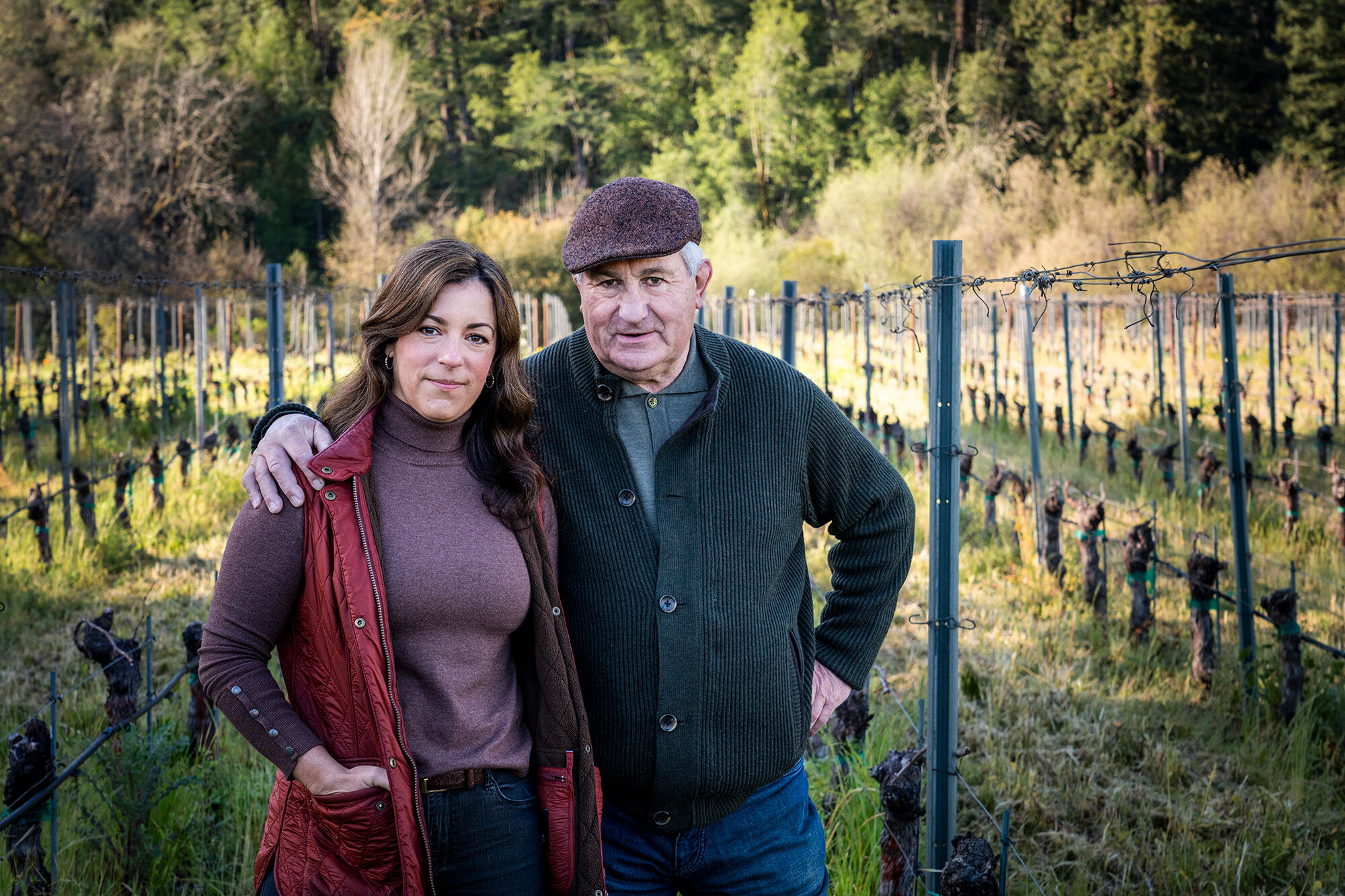 A man and a woman in a vineyard with bare vines looking at the camera.